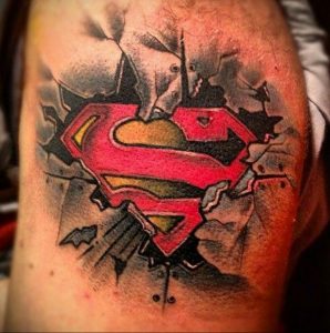Фото тату на руке с изображением логотипа Superman, как будто прорвавшего стену. Цветной рисунок татуировки.