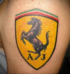 Фото тату на плече с изображением логотипа Ferrari – скачущей лошади на желтом фоне. Черно-белый рисунок татуировки.