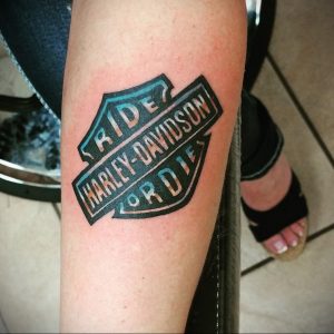 Фото тату логотипа Harley-Davidson с надписью 'Ride or Die'. Цветной рисунок татуировки, расположен на предплечье.