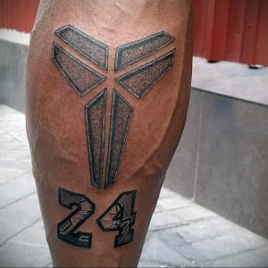 Черно-серая татуировка на ноге с изображением номера 24 и символа Кобе Брайанта, выполненная в графичном стиле.