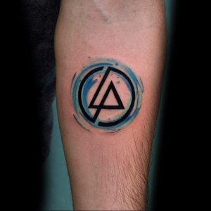 Фото тату на руке: небольшая акварельная татуировка с логотипом группы Linkin Park в круге, выполненная в голубых тонах. Простой и стильный дизайн.