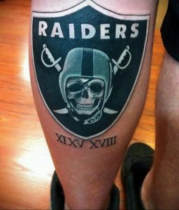 Фото тату логотипа команды Raiders на ноге. Черно-белый рисунок с детальной проработкой шлема и скрещенных мечей. Идеально для фанатов американского футбола.