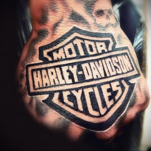 Фото тату логотипа Harley-Davidson на груди. Черно-белый рисунок, детализированная прорисовка, классический дизайн. Подходит для настоящих байкеров.