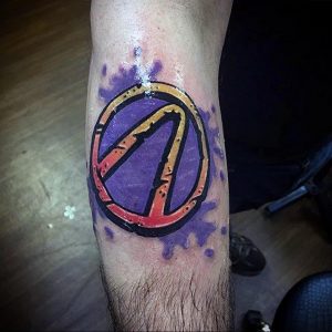 Фото тату логотипа Borderlands на икре. Яркие цвета, фиолетовый фон, оранжевый символ. Подходит для поклонников шутера Borderlands.