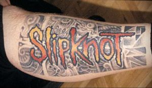 Фото тату с надписью Slipknot, выполненной в ярких оранжево-красных тонах на фоне серо-черного фона. Расположена на предплечье.