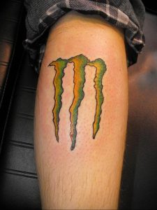 Фото тату логотипа Monster Energy на икре. Яркие цвета, градиент от желтого к зеленому, острые когти. Подходит для любителей экстремальных видов спорта.