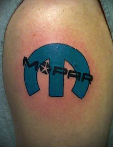Фото тату логотипа Mopar на плече. Яркий синий цвет, четкие контуры, классический дизайн. Подходит для поклонников автомобилей Chrysler, Dodge, Jeep и Ram.