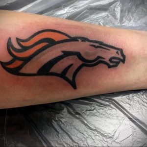 Фото тату на руке с изображением логотипа команды Denver Broncos. Черный, оранжевый и белый цвета, четкий контур.