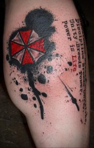 Фото тату на руке с изображением красного зонта Umbrella Corporation из Resident Evil. Рисунок татуировки в стиле аниме с брызгами краски.