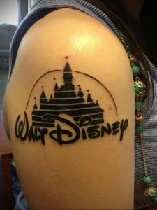 Фото тату на плече с изображением замка Диснея и надписи 'Walt Disney'. Черно-белый рисунок татуировки в мультяшном стиле.