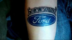 Фото тату на руке с изображением логотипа Ford и номером. Рисунок татуировки в синих и серых тонах.