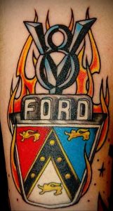 Фото тату с изображением двигателя Ford V8 в окружении языков пламени. Яркий и динамичный рисунок татуировки, выполненный в стиле old school.