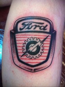 Фото тату с изображением логотипа Ford на руке. Черно-красный рисунок татуировки, выполненный в традиционном стиле.