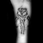 Фото тату мандалорского черепа на предплечье, выполненное в черно-серых тонах с использованием техники светотени для создания эффекта объема и реалистичности.