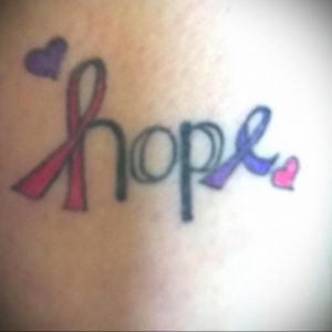 Фото тату: татуировка с надписью 'Hope' и двумя лентами – розовой и фиолетовой – с маленькими сердечками.
