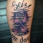 Фото тату на ноге с фиолетовой лентой, обвитой шипами, и надписью 'Seize the day'. Символ борьбы и стремления к жизни.