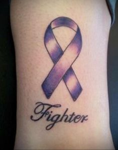 Фото тату фиолетовой ленты на руке с надписью 'Fighter'. Символ поддержки и борьбы с болезнью, выполненный в реалистичном стиле.