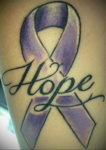 Фото тату: фиолетовая лента надежды с надписью 'Hope', расположенная на плече. Символ веры и поддержки.