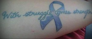 Фото тату: голубая лента с надписью 'With struggle comes strength' на руке, символ преодоления трудностей.