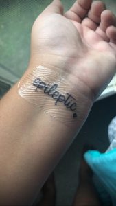 Фото татуировки на запястье: минималистичная надпись 'Epileptic' черным цветом. Простой и информативный рисунок.