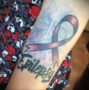 Фото акварельной татуировки с изображением фиолетовой ленты и надписи 'Epilepsy'. Нежные цвета, размытые контуры, символическое значение. Идея для тату, посвященной борьбе с эпилепсией.