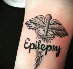 Фото татуировки с надписью 'Epilepsy' и символом Эскулапа (змея, обвивающая посох). Черно-белый рисунок, детальная проработка, реалистичный стиль. Идея для тату, посвященной борьбе с эпилепсией.