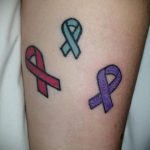 Фото тату на руке: три небольшие ленты разных цветов (красная, бирюзовая, фиолетовая). Символизируют поддержку различных заболеваний и проблем.