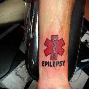 Фото тату: красная звезда жизни с надписью 'Epilepsy' на руке, выполненная в простом, но информативном стиле. Важная татуировка для людей с эпилепсией.