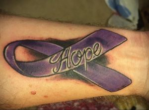 Фото тату на руке: фиолетовая лента с надписью 'Hope', символизирующая надежду и поддержку.