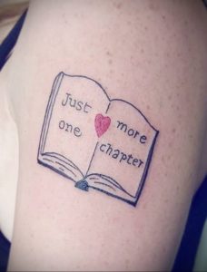 Фото тату на плече с изображением открытой книги и красного сердца. Надпись "Just one more chapter" добавляет татуировке индивидуальности.