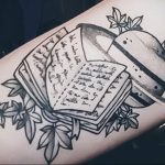 Фото тату на руке: открытая книга и планета Сатурн, черно-белая татуировка, детализированный рисунок. Оригинальный и символичный образ.