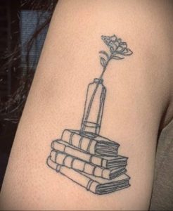 Фото тату на руке: стопка книг, ваза с цветком, черно-белая татуировка, минималистичный стиль. Простой и элегантный рисунок.