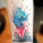 Фото тату на руке: раскрытая книга, из которой вырывается звездное небо, выполнена в акварельной технике. Красивый рисунок татуировки для мечтателей и любителей космоса.
