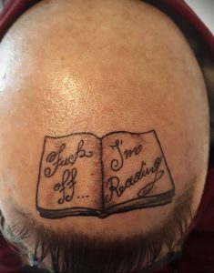 Фото татуировки на голове с изображением открытой книги и надписи "Fuck I'm Reading".