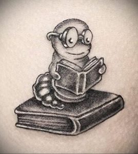 Фото татуировки с изображением милого книжного червя в очках, читающего книгу на стопке книг.