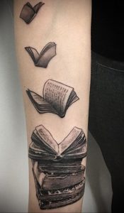 Фото татуировки в стиле минимализм, изображающей несколько открытых книг, словно парящих в воздухе, на руке.