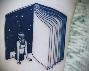 Фотография татуировки на руке с изображением раскрытой книги, внутри которой находится человек, смотрящий на звездное небо.