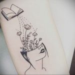 Фотография татуировки на руке с изображением раскрытой книги, из которой растут цветы внутри головы человека.