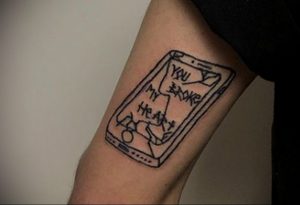Фото тату на руке с изображением разбитого смартфона и надписью 'You broke my heart'. Черно-белый рисунок татуировки в минималистичном стиле.