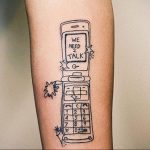 Черно-белое фото тату на руке с изображением старого телефона и фразой "WE NEED 2 TALK". Стиль татуировки - графика.