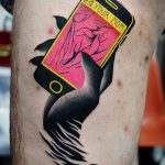 Фото тату на предплечье: смартфон с сообщением 'YOUR MOM' и черным вороном, взлетающим из разбитого экрана. Яркие цвета и динамичная композиция.