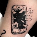 Черно-белое фото татуировки на руке с изображением разбитого экрана смартфона iPhone. Реалистичный рисунок татуировки, передающий ощущение хрупкости.