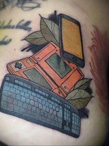Цветная татуировка на руке с изображением смартфона, Game Boy и клавиатуры. Символическая татуировка, отражающая любовь к технологиям и ретро-играм.