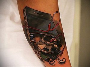 Реалистичная татуировка на предплечье, изображающая смартфон и стетоскоп. Символическое изображение, сочетающее технологии и медицину.