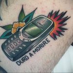 Фото тату на руке: старый телефон Nokia с цветами и надписью 'Duro A Morire'. Рисунок татуировки в стиле олдскул.
