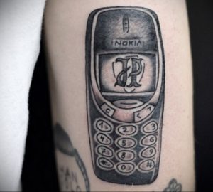 Фото тату на руке: старый телефон Nokia с логотипом 'RP' на экране. Черно-белый рисунок татуировки в реалистичном стиле.