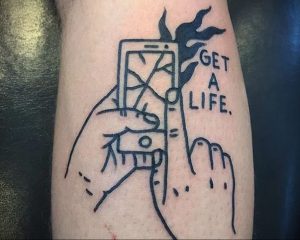 Фото тату руки, держащей разбитый телефон, с надписью 'GET A LIFE', выполненное в черно-белой графике, символизирующее протест против зависимости от гаджетов.