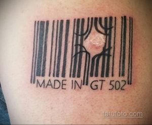 Фото тату штрих-кода с надписью 'MADE IN GT 502' на плече. Черный рисунок, четкие линии, минималистичный стиль.