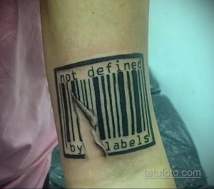 Фото тату на предплечье: штрихкод, разорванный острым когтем, с надписью 'not defined by labels'. Символизирует отказ от социальных ярлыков.
