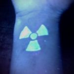 Фотография светящейся в темноте татуировки с символом радиации на запястье. Яркий, неоновый рисунок татуировки.